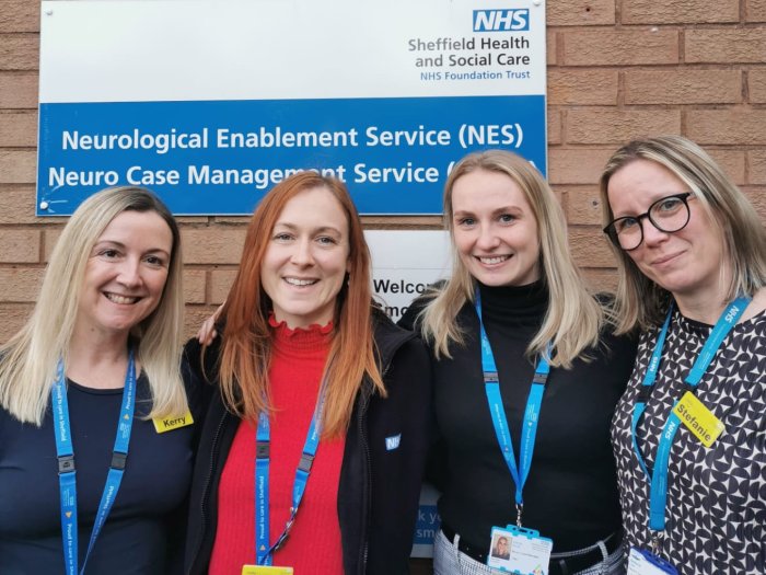 Neuro Case Management Service team members stood in front of an NHS building sign