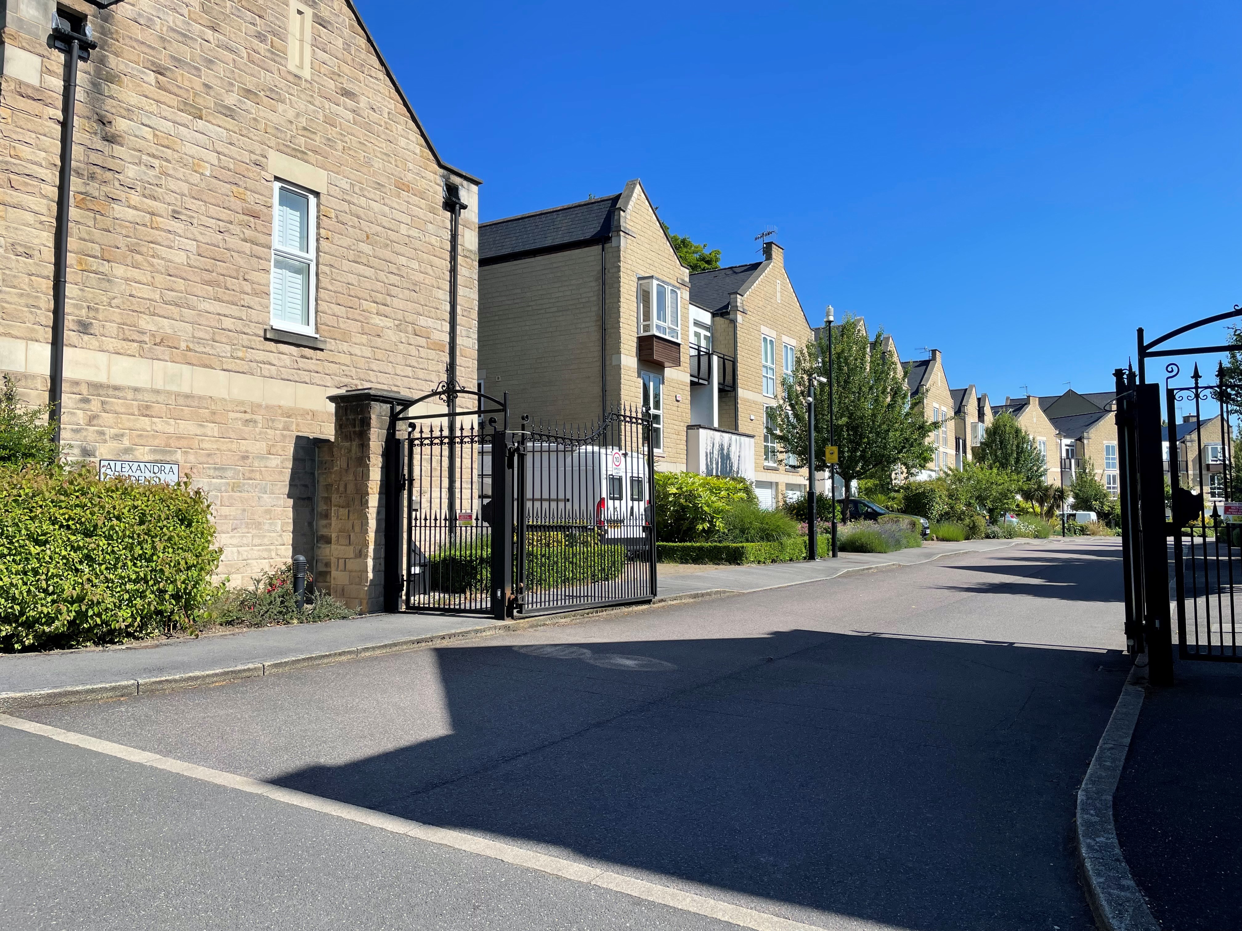 Image shows a gated road with pale brick houses and trees alongside