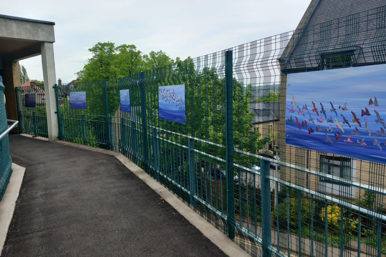 The bridge to the Porterbrook clinic with the 'art on the bridge' hanging up - these are paintings of different coloured birds taking flight in a blue sky.