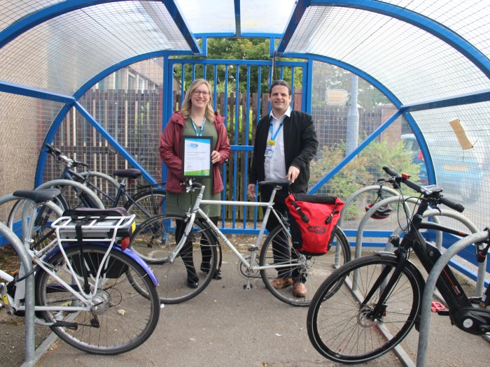 Two people stand in a bike shelter holding a certificate